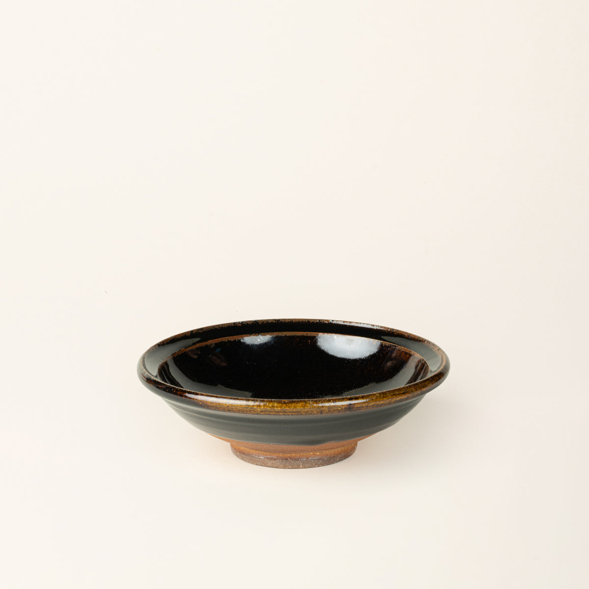 A small handmade ceramic bowl with a wood fired earthy muddy glaze and an unglazed base.