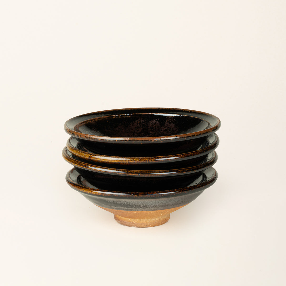 A stack of 4 small handmade ceramic bowls with a wood fired earthy muddy glaze and an unglazed base.