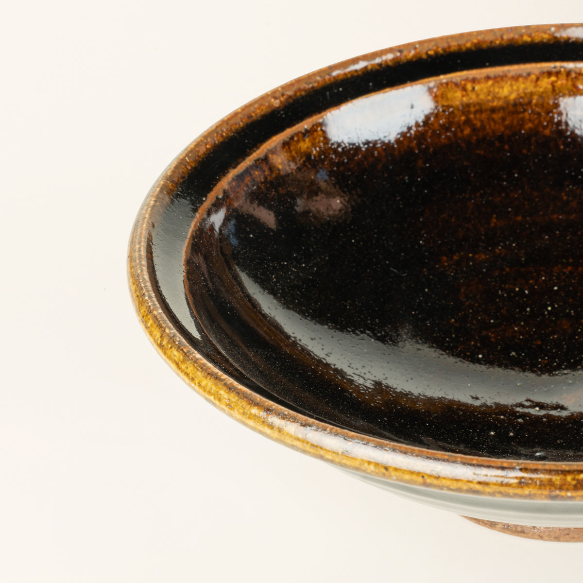 Closeup of a small handmade ceramic bowl with a wood fired earthy muddy glaze and an unglazed base.