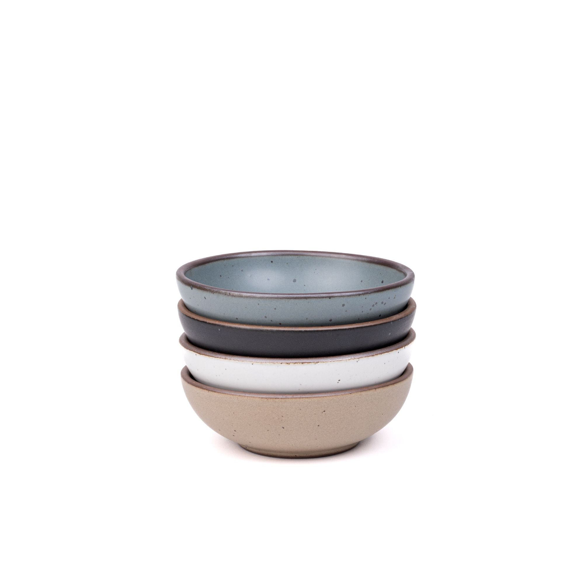 A stack of 4 small shallow ceramic bowls in a blue-grey, graphite black, cool white, and warm pale brown colors featuring iron speckles and an unglazed rim