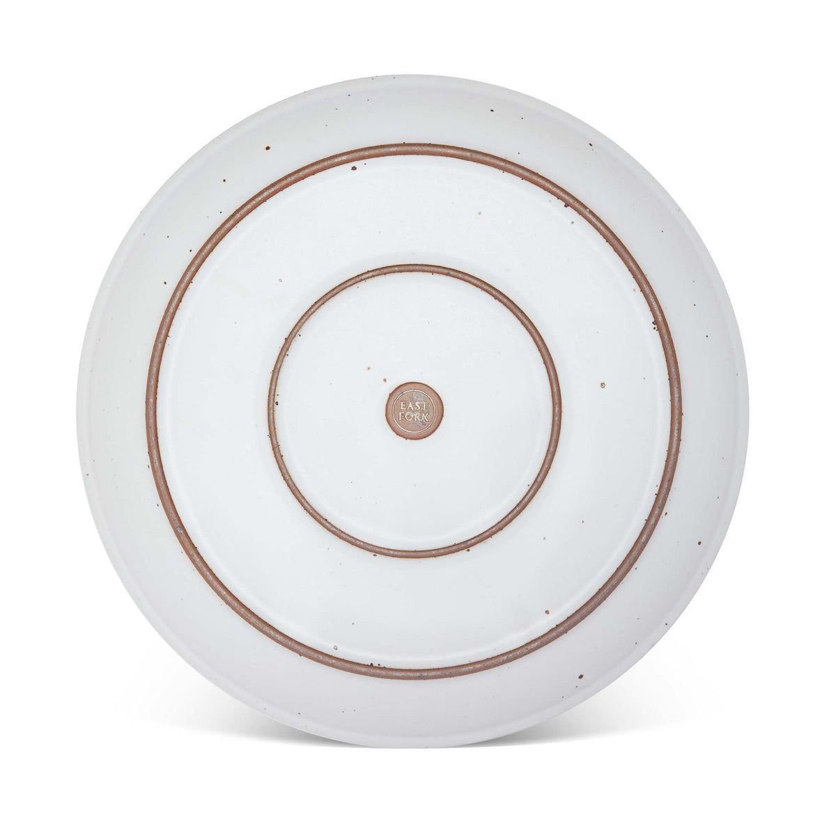 The bottom of a large ceramic platter in a cool white color featuring iron speckles and an unglazed rim.