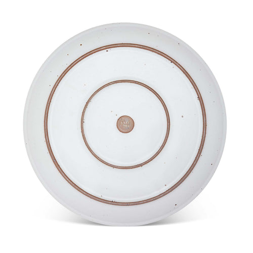 The bottom of a large ceramic platter in a cool white color featuring iron speckles and an unglazed rim.