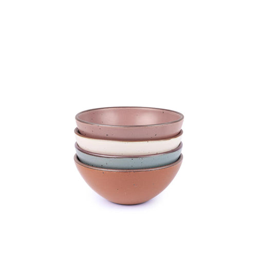 A stack of 4 medium sized rounded ceramic bowls in a cool terracotta, warm off-white, blue-grey and dusty mauve pink colors featuring iron speckles and an unglazed rim