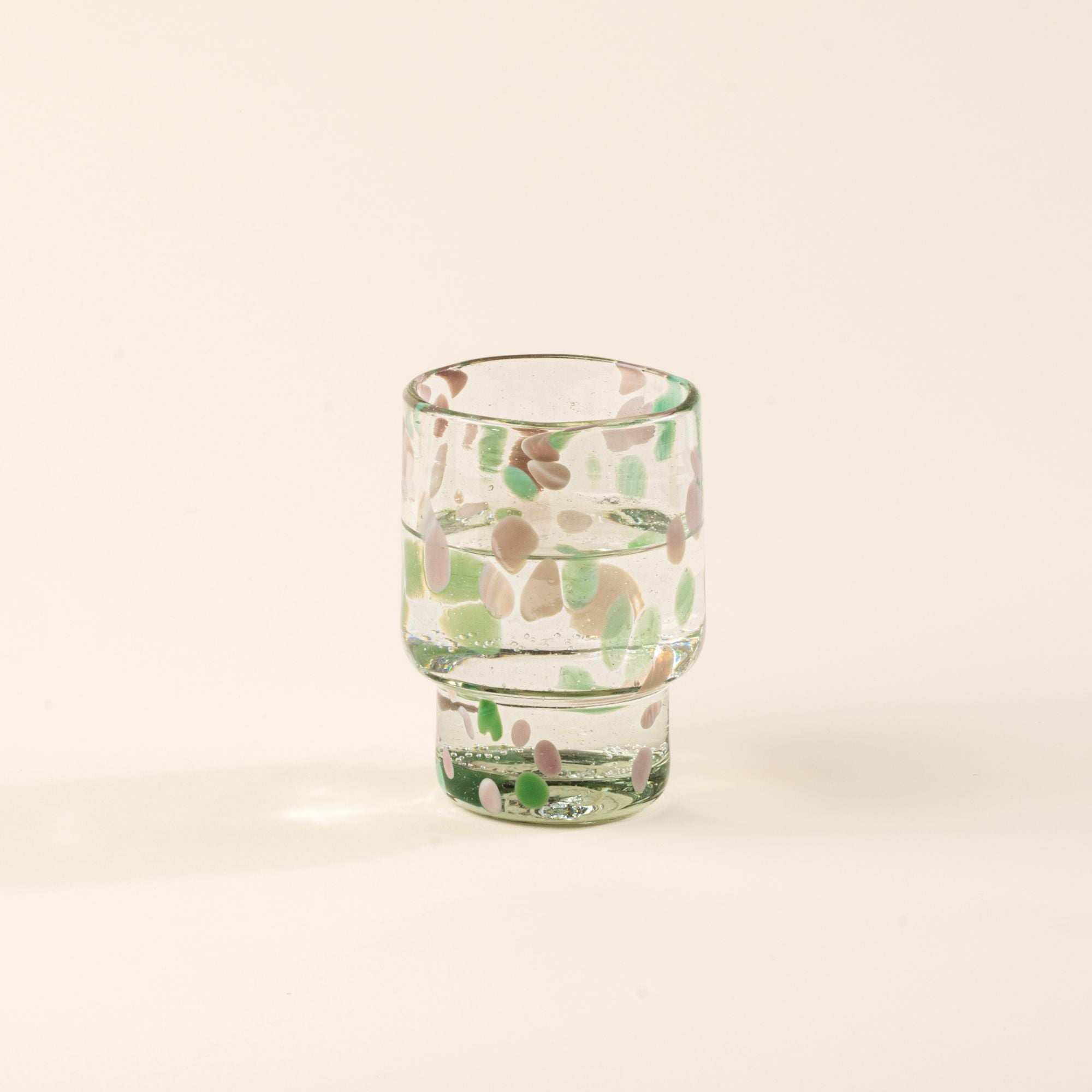A short clear glass with pastel green and pink speckled patterns, filled with water
