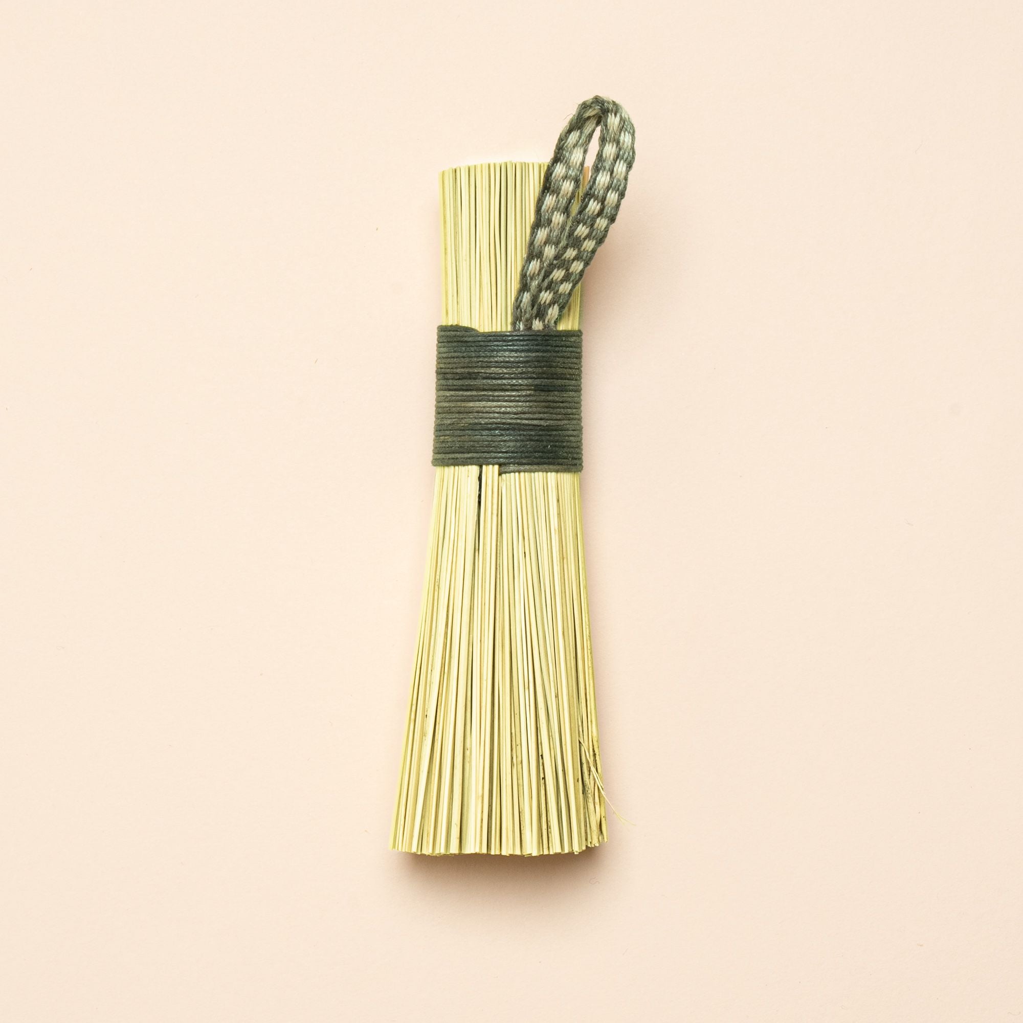 A short scrub made out of broomcorn, tied together with cotton and a loop for hanging.