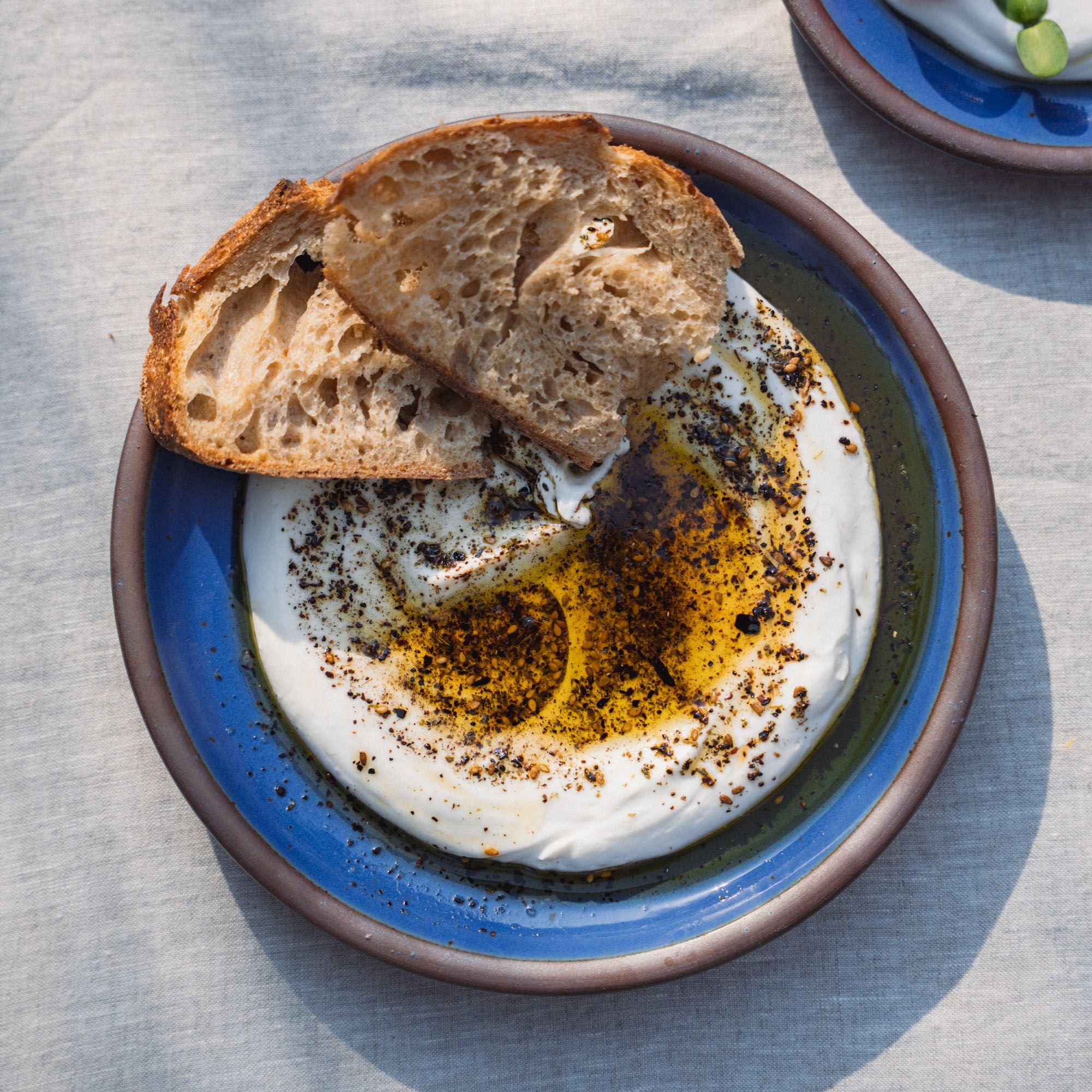 A medium sized plate in a cobalt blue color with a dip and olive oil, and 2 pieces of bread.
