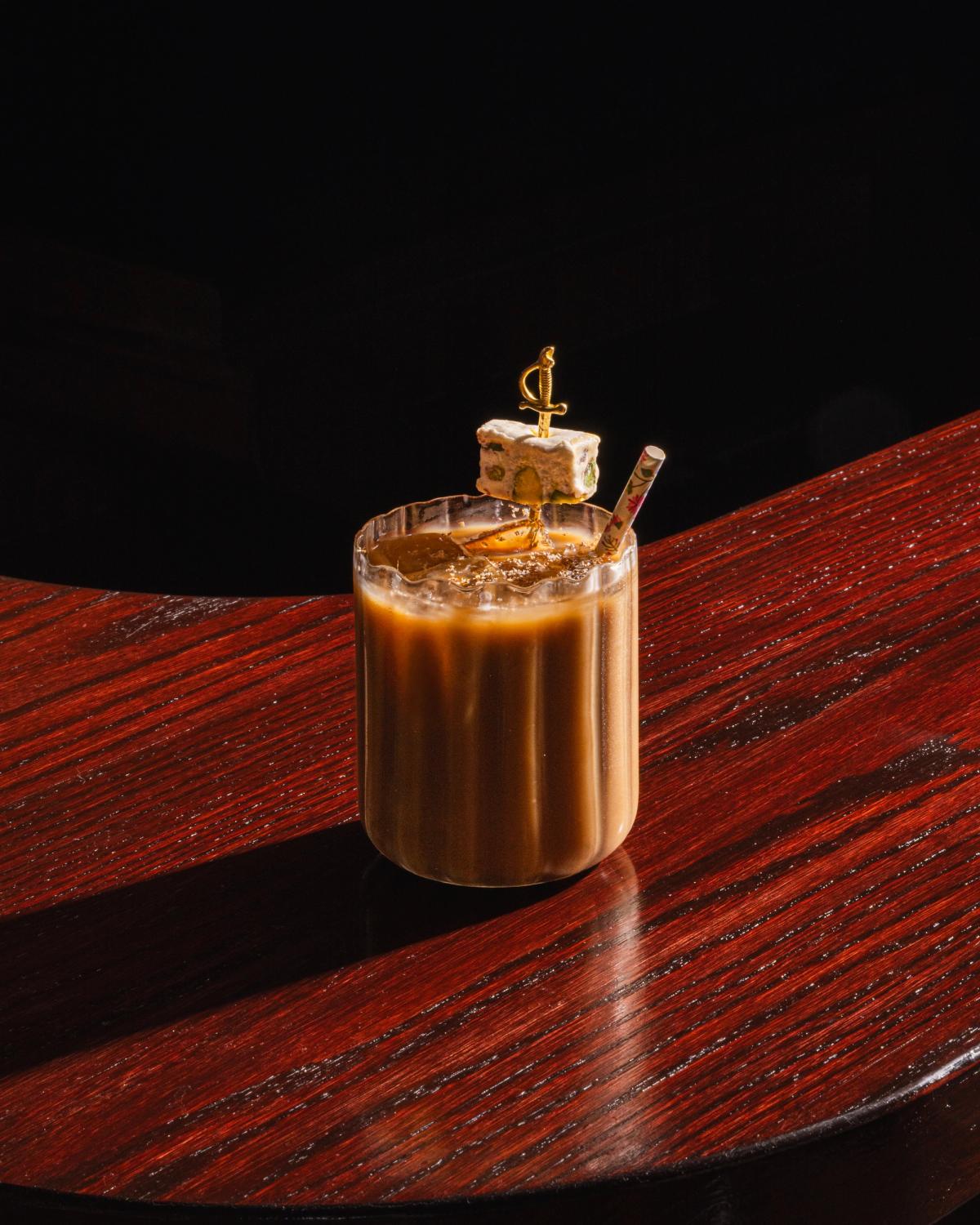 A creamy, brown cocktail in a fluted clear glass sits on a dark wood counter.