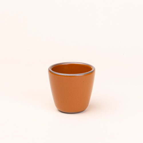 A short cup that tapers out to get wider at the top in an earthy orange color featuring iron speckles