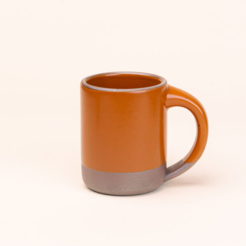 A big sized ceramic mug with handle in an earthy orange color featuring iron speckles and unglazed rim and bottom base.