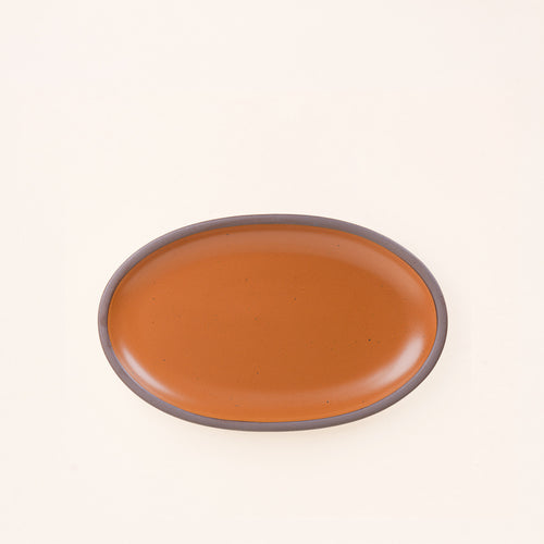 A medium oval ceramic platter in an earthy orange color featuring iron speckles and an unglazed rim