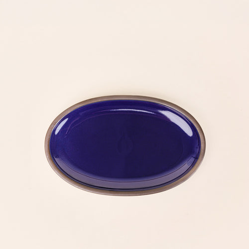A medium oval ceramic platter in a glossy dark blue color featuring iron speckles and an unglazed rim