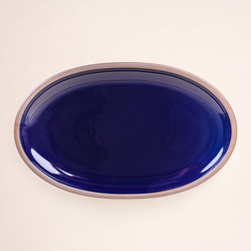A large oval ceramic platter in a glossy dark blue color featuring iron speckles and an unglazed rim