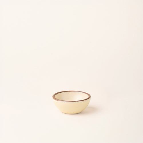 A tiny rounded ceramic bowl in a cream color featuring iron speckles and an unglazed rim