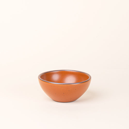 A small dessert sized rounded ceramic bowl in an earthy orange color featuring iron speckles and an unglazed rim
