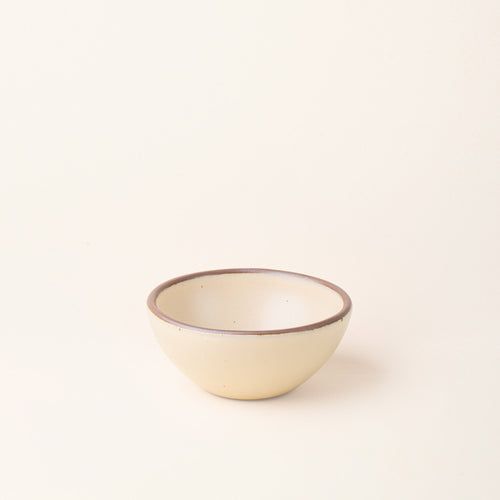 A small dessert sized rounded ceramic bowl in a cream color featuring iron speckles and an unglazed rim
