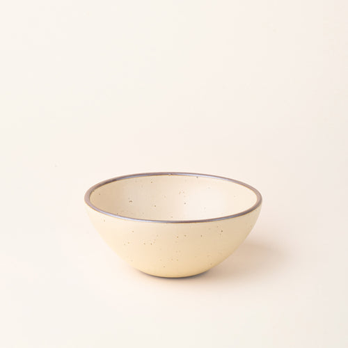 A medium rounded ceramic bowl in a cream color featuring iron speckles and an unglazed rim