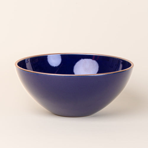 A large ceramic mixing bowl in a glossy dark blue color featuring iron speckles and an unglazed rim