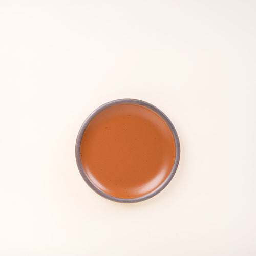 A dessert sized ceramic plate in an earthy orange color featuring iron speckles and an unglazed rim.