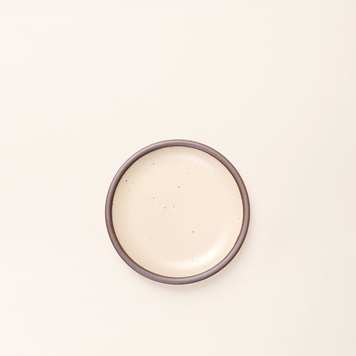 A dessert sized ceramic plate in an cream color featuring iron speckles and an unglazed rim.
