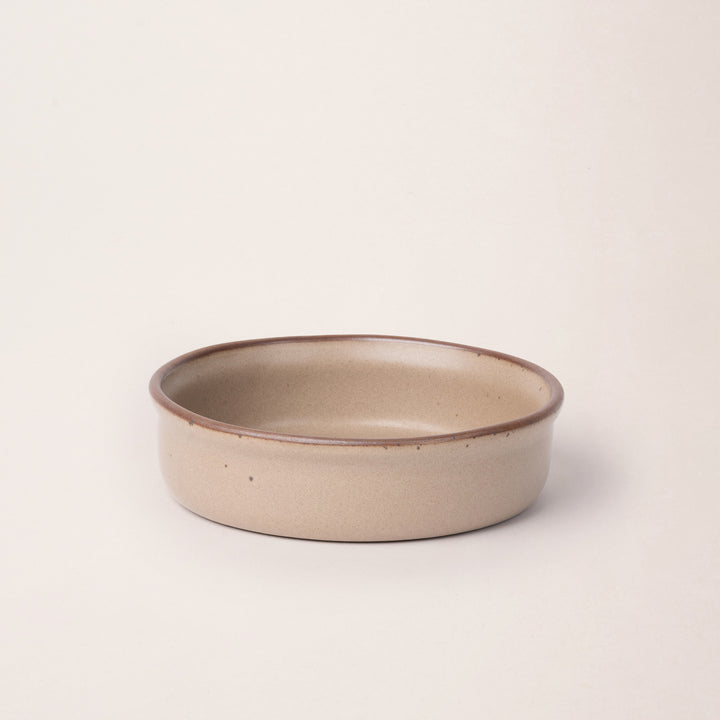 Wide shallow ceramic ramekin in a warm pale brown color with an unglazed rim