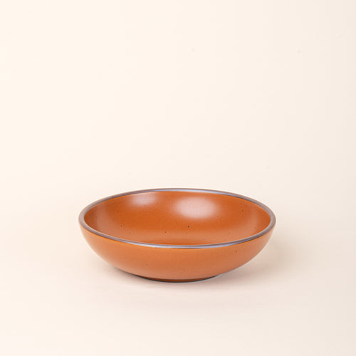 A dinner-sized shallow ceramic bowl in an earthy orange color featuring iron speckles and an unglazed rim