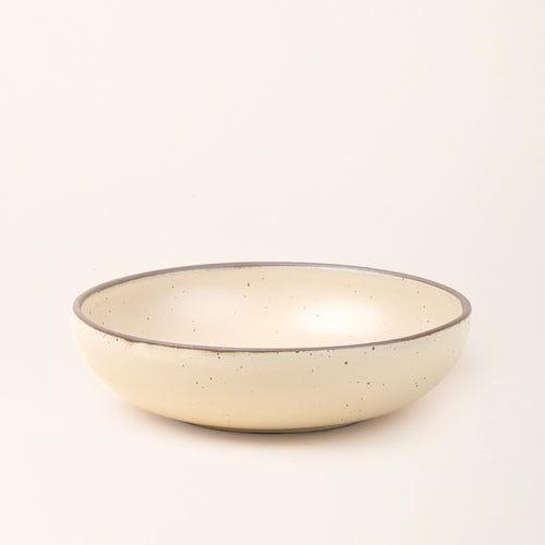 A large shallow serving ceramic bowl in a cream color featuring iron speckles and an unglazed rim.