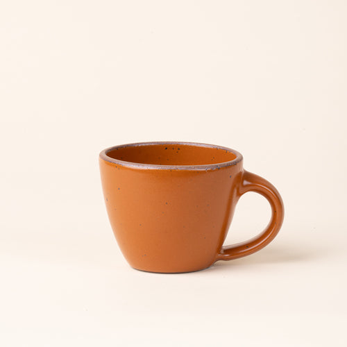 Round stoneware mug with handle, in an earthy orange color with iron speckles and an unglazed rim.