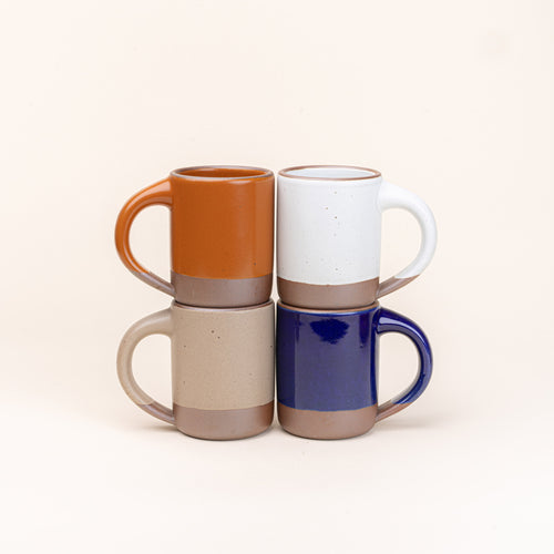 Four medium sized ceramic mugs with handles in an earthy orange, glossy dark blue, graphite black, and warm pale brown colors featuring iron speckles and unglazed rim