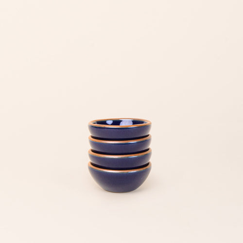 A stack of 4 tiny rounded ceramic bowls in a glossy dark blue color featuring iron speckles and an unglazed rim
