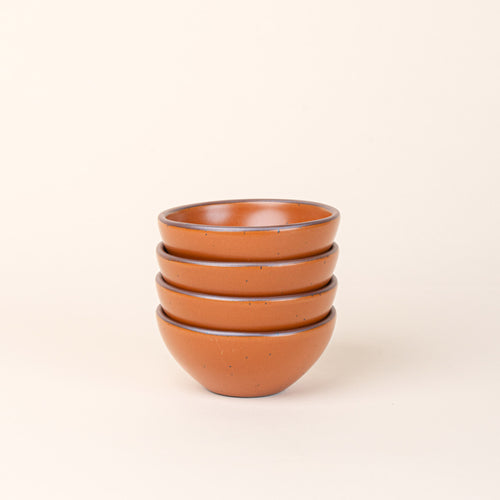 A stack of 4 small dessert sized rounded ceramic bowls in an earthy orange color featuring iron speckles and an unglazed rim