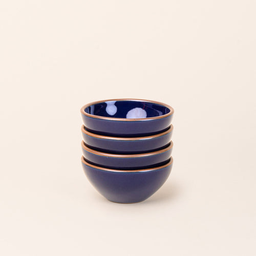 A stack of 4 small dessert sized rounded ceramic bowls in a glossy dark blue color featuring iron speckles and an unglazed rim
