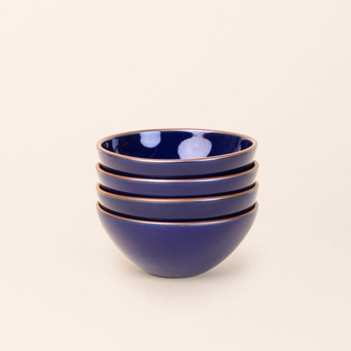 A stack of 4 medium rounded ceramic bowls in a glossy dark blue color featuring iron speckles and an unglazed rim