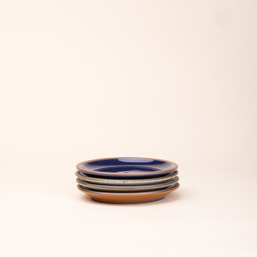 4 dessert sized ceramic plates in a glossy dark blue, earthy orange, warm pale brown and white colors featuring iron speckles and an unglazed rim