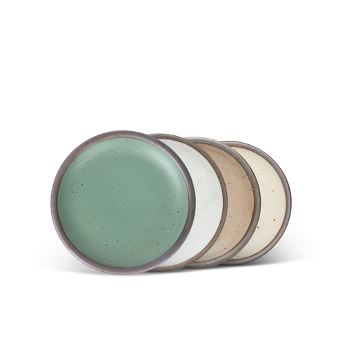 Four ceramic plates with flat surfaces and raised edges in a viridian green, warm brown, warm white and cool white glazes.