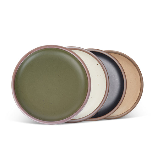 4 medium sized ceramic plates in an olive green, graphite black, warm pale brown, and off-white colors featuring iron speckles and an unglazed rim.