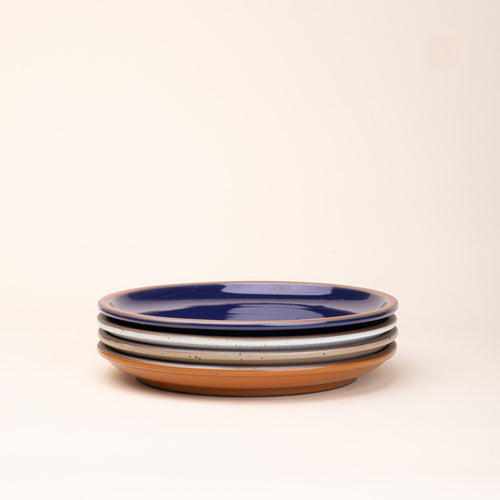 4 dinner sized ceramic plates in a glossy dark blue, earthy orange, warm pale brown and white colors featuring iron speckles and an unglazed rim