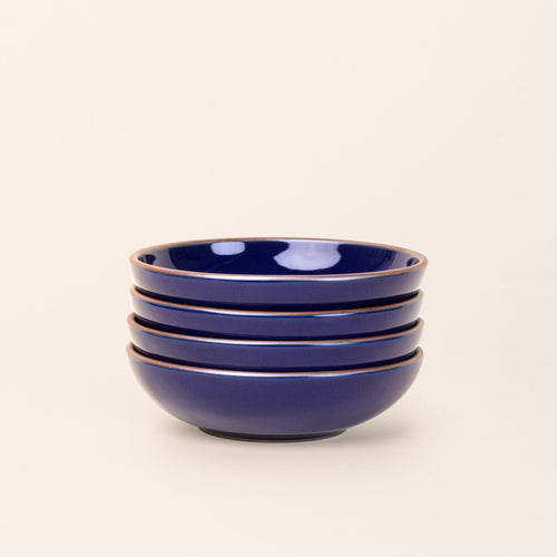 A stack of 4 dinner-sized shallow ceramic bowls in a glossy dark blue color featuring iron speckles and an unglazed rim