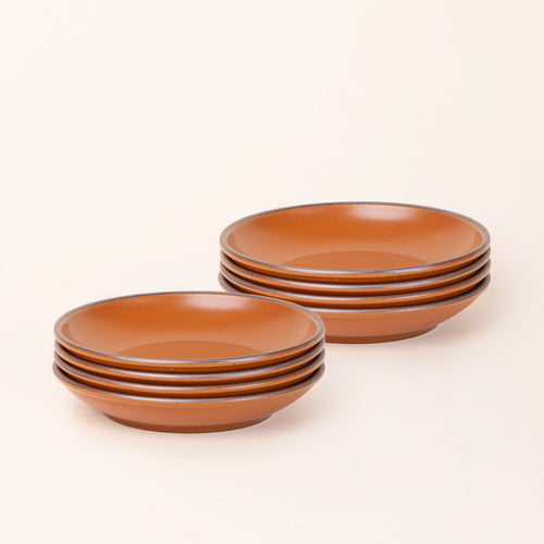 2 stacks of 4 medium ceramic plates with a curved bowl edge in an earthy orange color featuring iron speckles and an unglazed rim.
