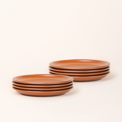 2 stacks of 4 medium sized ceramic plates in an earthy orange color featuring iron speckles and an unglazed rim.