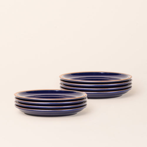 2 stacks of 4 medium sized ceramic plates in a glossy dark blue color featuring iron speckles and an unglazed rim.