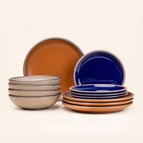 4 ceramic dinner plates in earthy orange, 4 side plates in glossy dark blue, and 4 shallow dinner bowls in pale warm brown with iron speckles and unglazed rims.