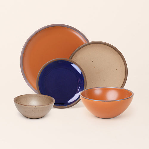 An ice cream bowl, soup bowl, cake plate, side plate and dinner plate paired together in earthy orange, pale warm brown and glossy dark blue colors featuring iron speckles