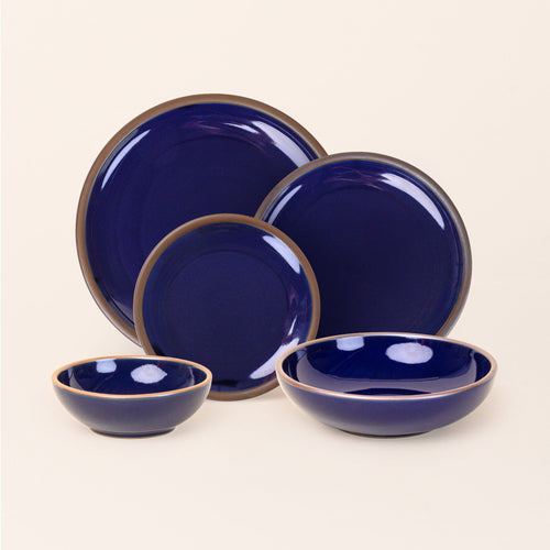 A breakfast bowl, everyday bowl, cake plate, side plate and dinner plate paired together in a glossy dark blue color featuring iron speckles