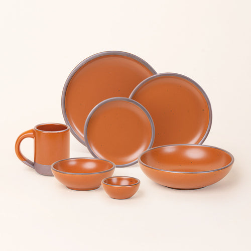 The Mug, bitty bowl, breakfast bowl, everyday bowl, cake plate, side plate and dinner plate paired together in an earthy orange color featuring iron speckles