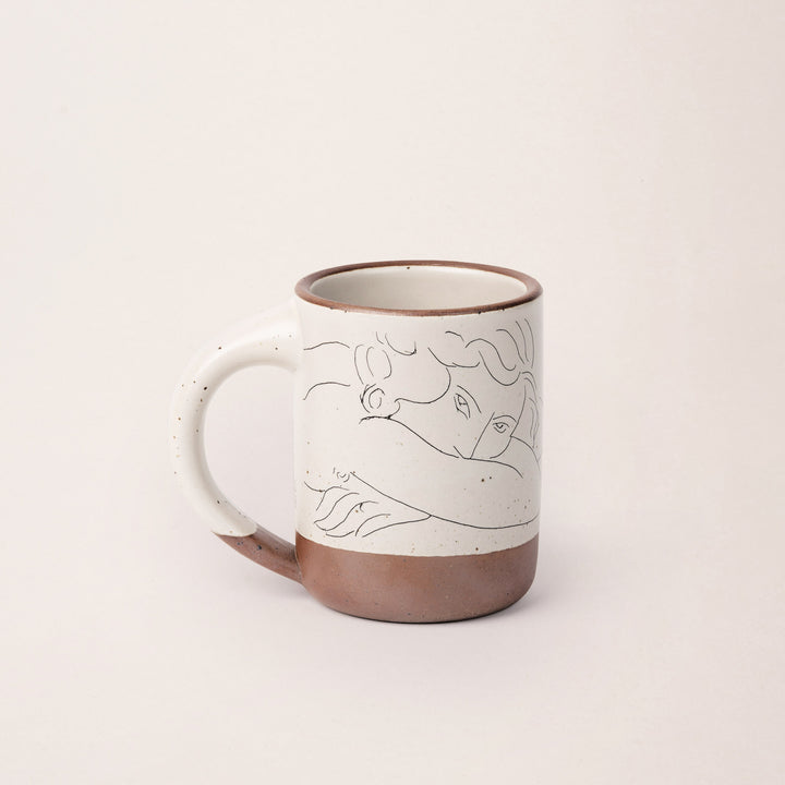 East Fork’s The Mug in a warm off white color with handle with a black decal of Henri Matisse’s Jeune femme la visage enfoui dans les bras, a bright blue, a line drawing of a young woman with face buried in her arms, on the body of the mug