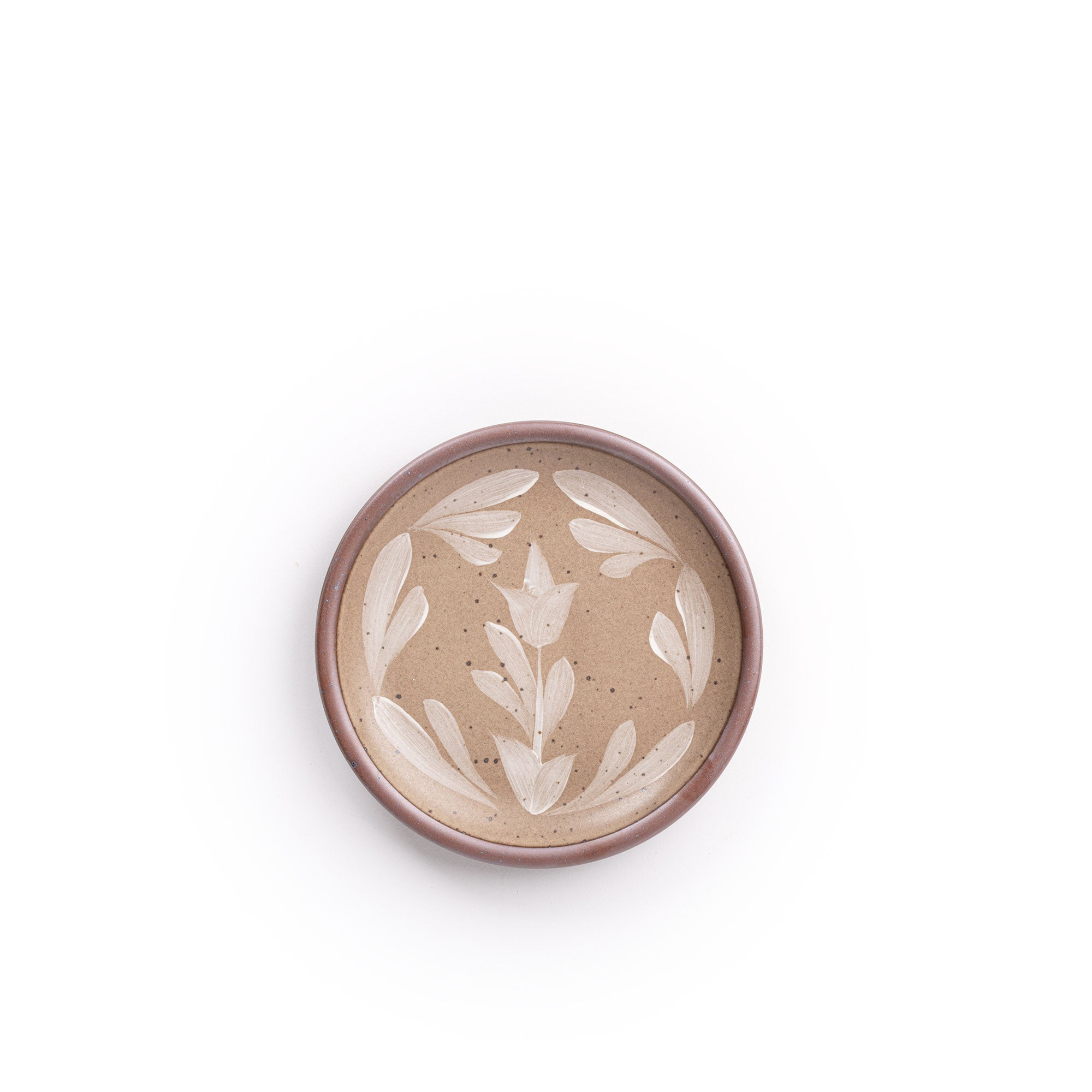 Small round ceramic plate with a hand-painted white flower and leaf design on a warm pale brown background with an exposed clay rim.