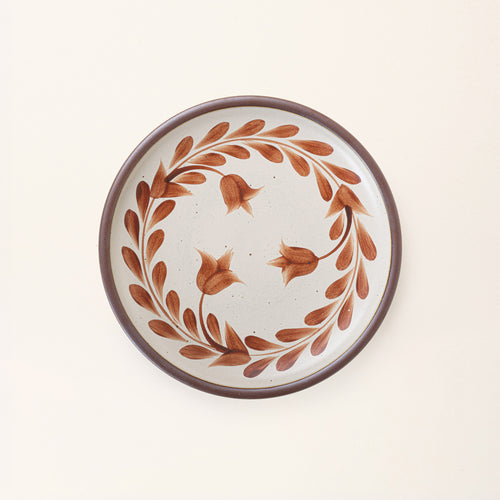 Dinner round ceramic plate with a hand-painted cool terracotta leaf wreath and floral design on a cream background with an exposed clay rim.