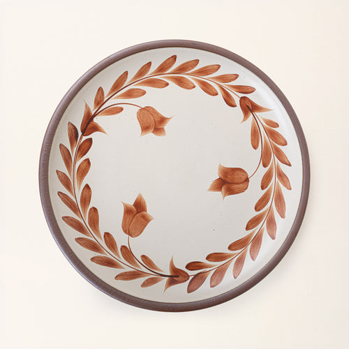 Large round ceramic platter with a hand-painted cool terracotta leaf wreath and floral design on a cream background with an exposed clay rim.