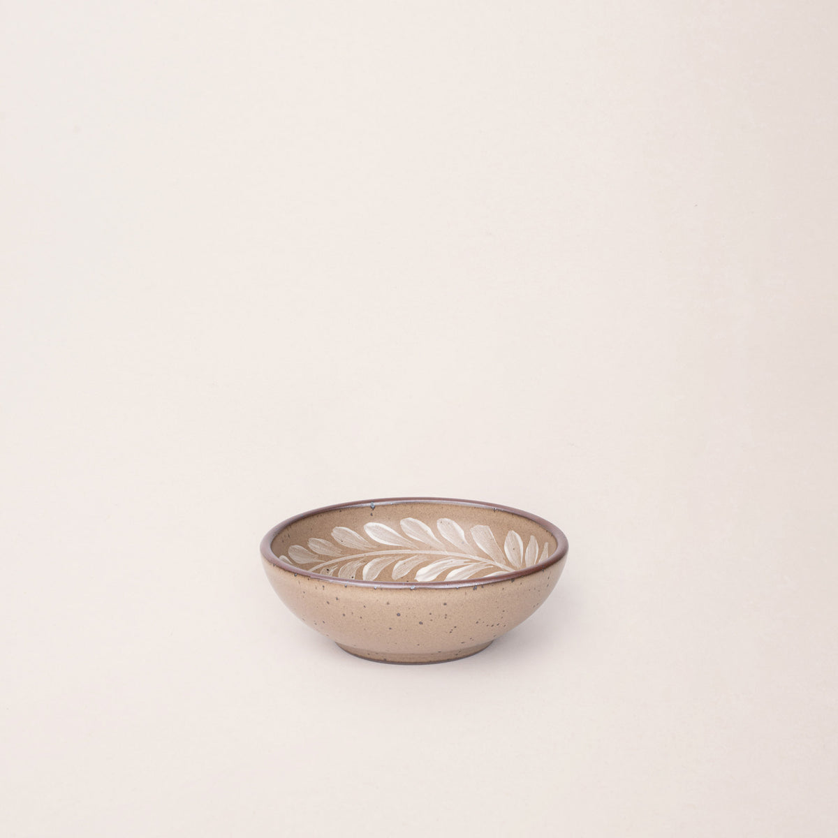 Small ceramic shallow bowl with a hand-painted white leaf border on a pale warm brown interior and exterior with an exposed clay rim.