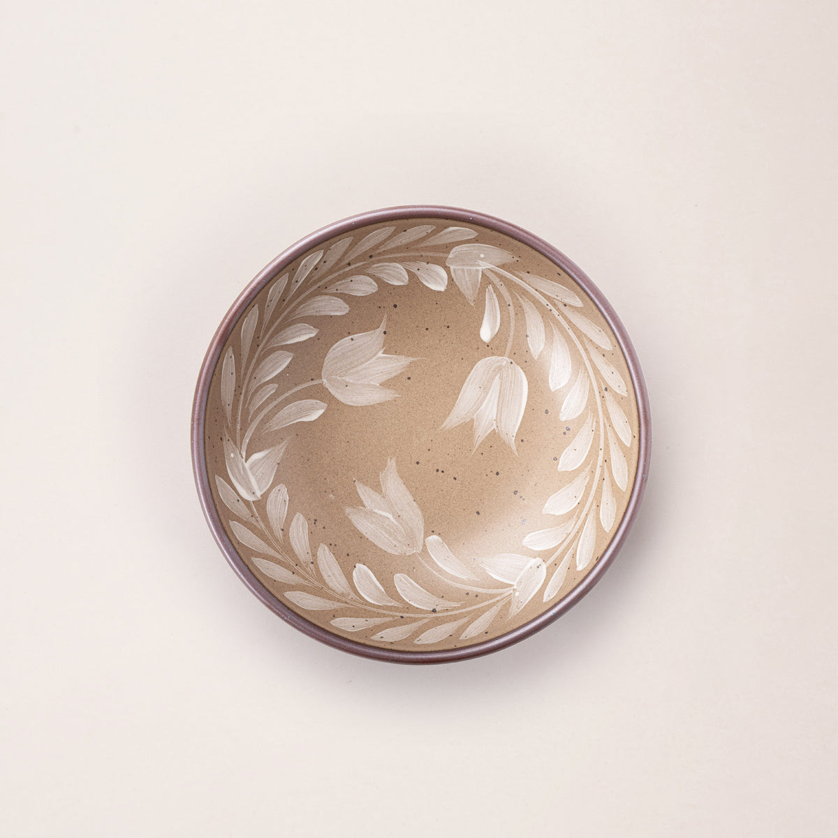 Overhead of a Medium ceramic shallow bowl with a hand-painted white leaf border on a pale warm brown interior and exterior with an exposed clay rim.